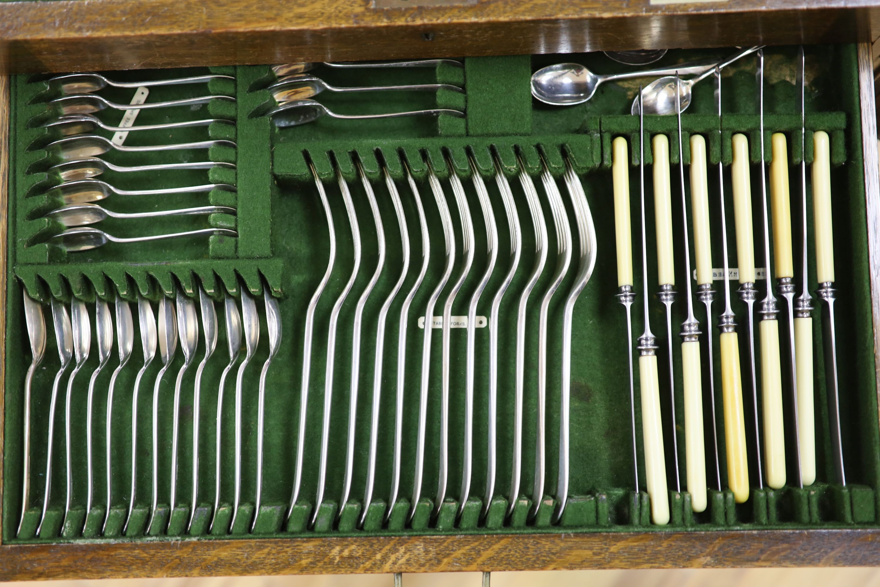 An Edwardian oak cased silver plated table canteen, settings for twelve and a set of silver plated fish knives and forks for twelve